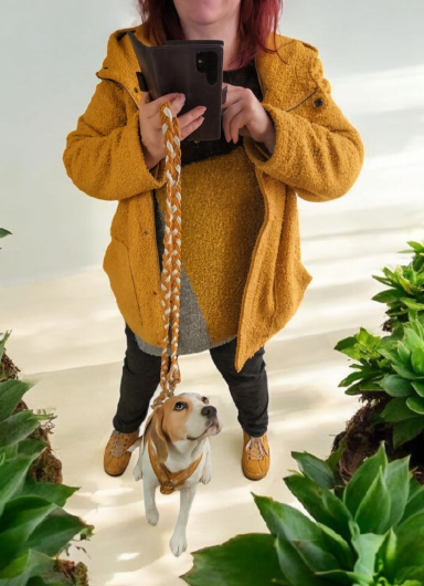 Frau mit braunem Hund auf Leine, umgeben von grünen Pflanzen.