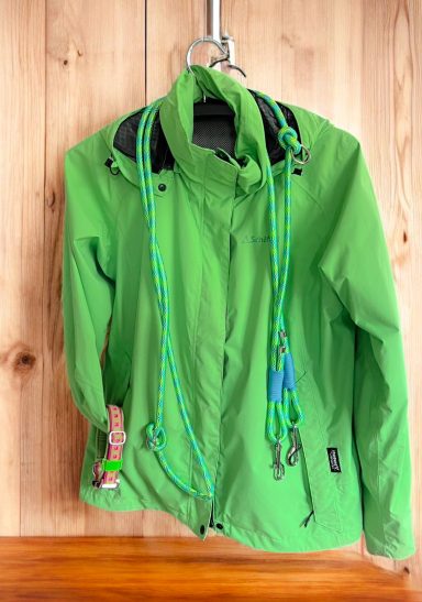 Grüne Jacke mit Kletterseilen an einer Holzwand aufgehängt.